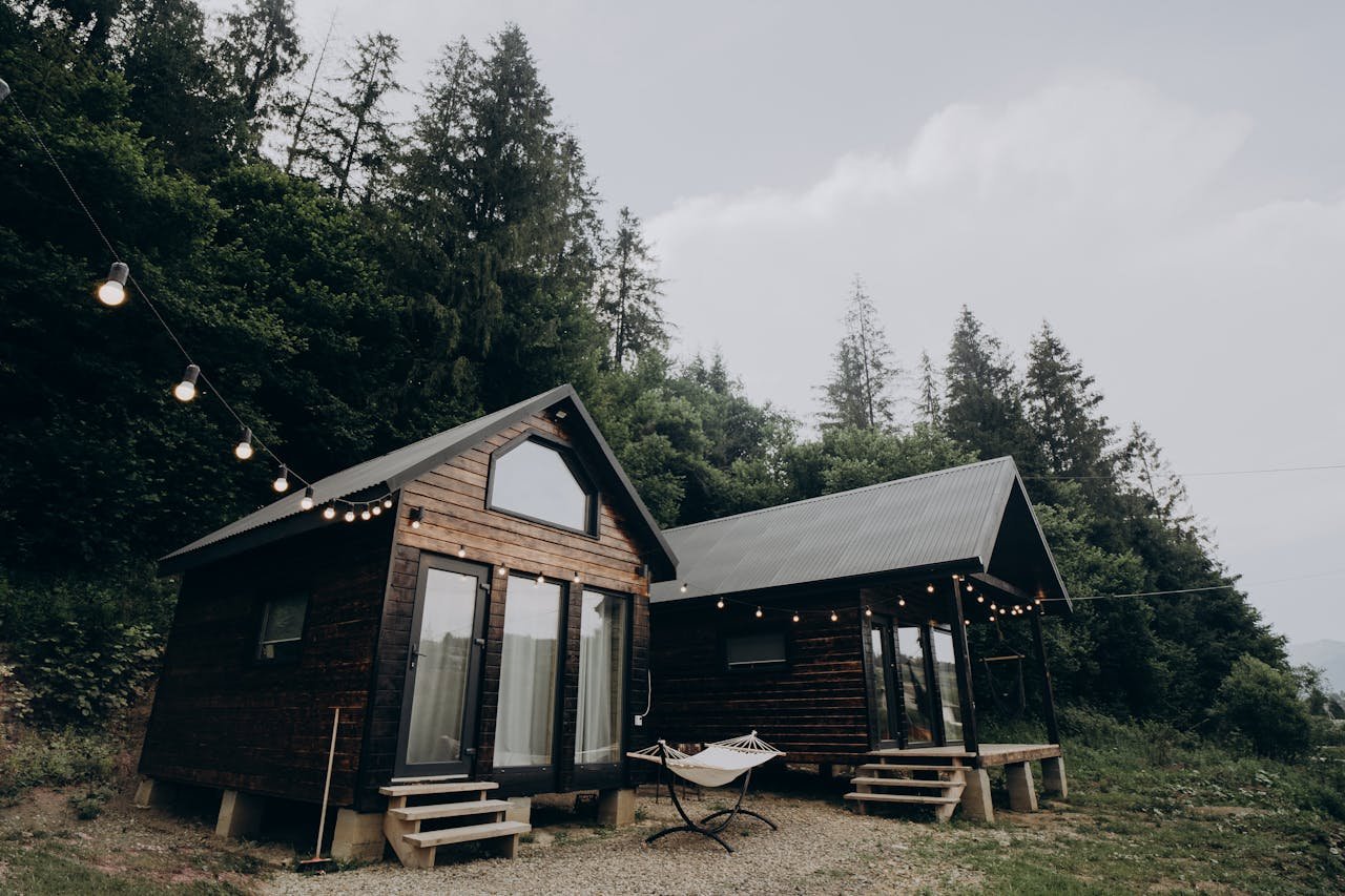Charming wooden cabins surrounded by lush forest with string lights at dusk, creating a serene and cozy atmosphere.